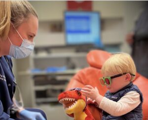 pediatric dentist teaching young child how to brush in dental chair